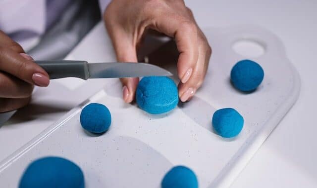 Person, die mit einem Messer blaue Badekugel schneidet.
